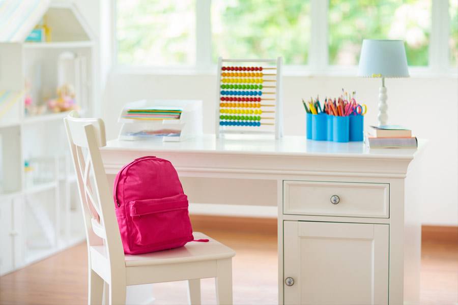 A white desk with a pink backpack sitting in a white chair